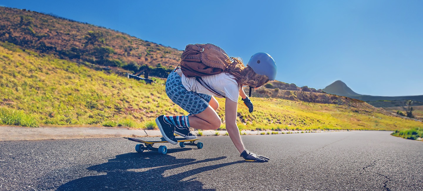 El longboarder está bajando por una carretera larga y vacía mientras es capturado por el fotógrafo que también está haciendo longboard por detrás. En la foto capturada, una línea a lo largo de la pantalla divide la foto en izquierda y derecha, lo que muestra la diferencia entre tomas estabilizadas y no estabilizadas.