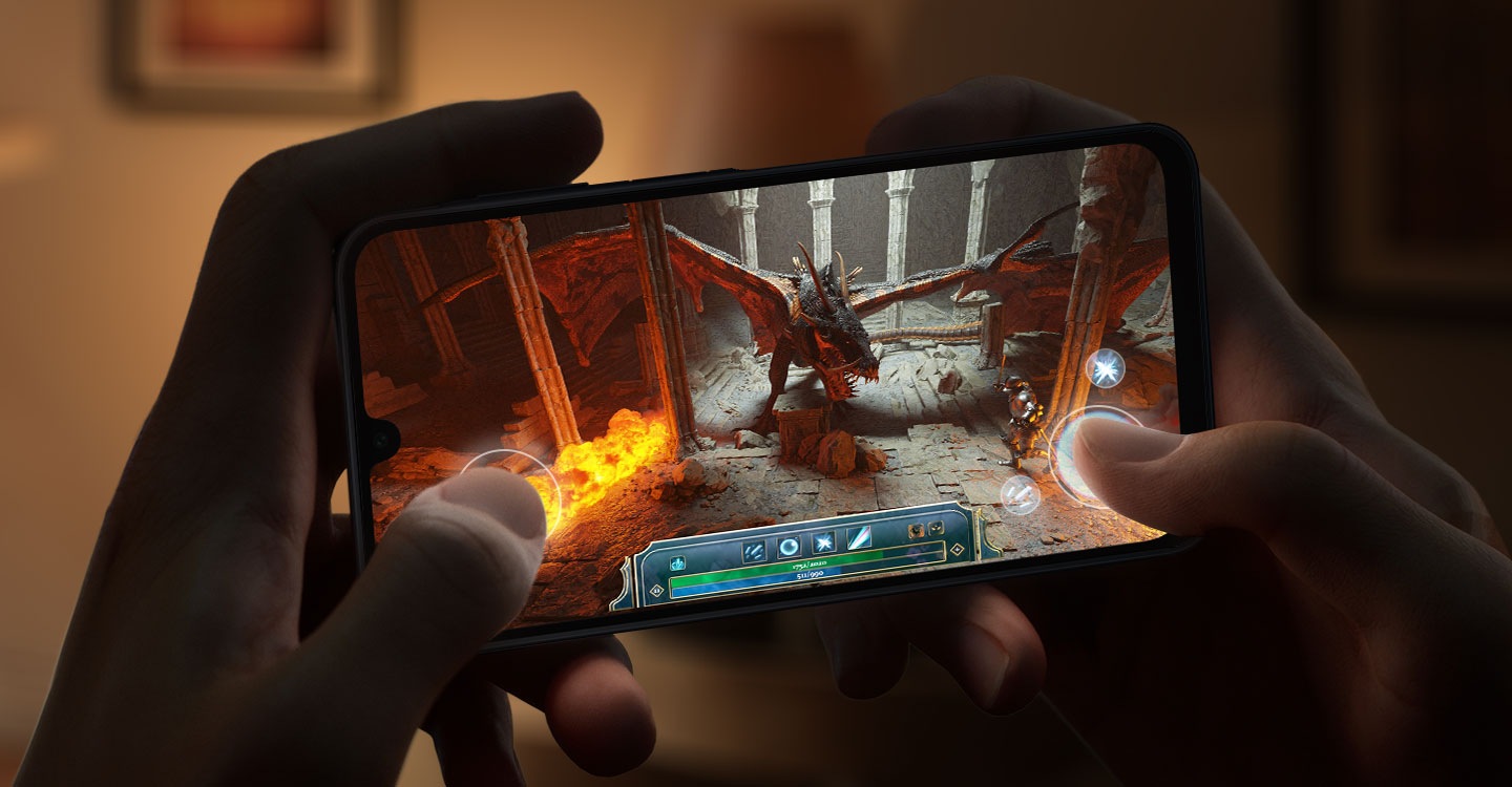Dos manos están agarrando un dispositivo Galaxy A16 5G para jugar un videojuego con muchos gráficos en una habitación con poca luz.