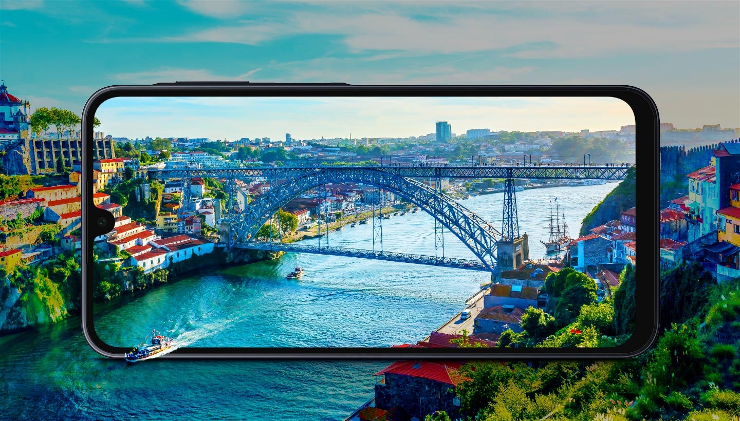 Ilustración de un paisaje urbano con un río que atraviesa y un puente que conecta ambos lados. Una pantalla grande del Galaxy A16 en el centro muestra una foto real de la escena. Aparece un bote en el río como si saliera de la pantalla, mostrando la calidad de pantalla envolvente del dispositivo.