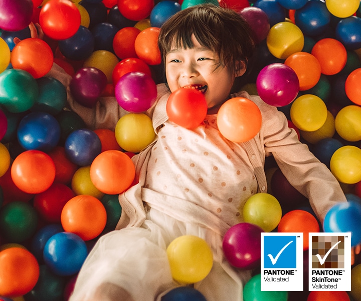 Un niño tumbado en una piscina de bolas de colores. Logotipo validado por Pantone™. Logotipo validado por Pantone™ SkinTone™.