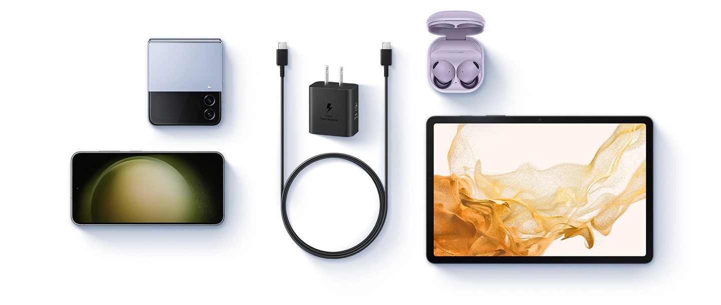 Se muestra una vista aérea de varios dispositivos con un adaptador de corriente negro y un cable USB-C colocado en el centro. A la izquierda, se muestran un Galaxy Z Flip4 azul y un Galaxy S23. A la derecha, se muestran Buds 2 Pro en Bora Purple y una Galaxy Tab S8.