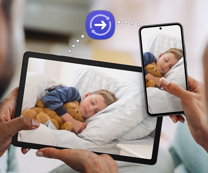 A couple is holding up Galaxy Tab A9+ and a Galaxy smartphone, both with the same photograph of a sleeping child onscreen. Above the devices is a dotted line that connects the devices, with the Quick Share icon in the middle to indicate the file-sharing feature.