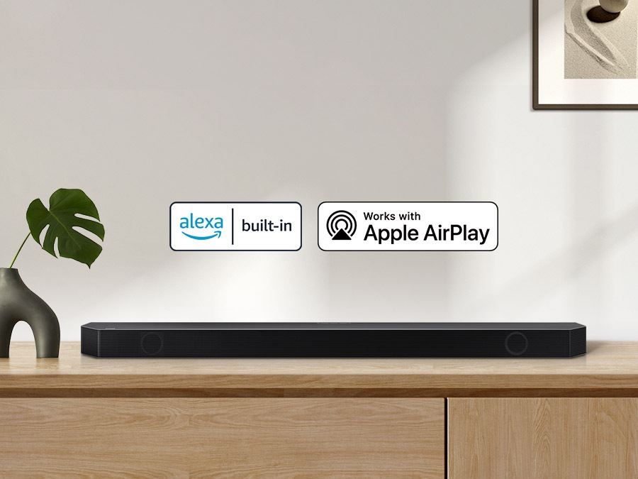 Alexa logo and Apple AirPlay logo can be seen along with Samsung Q990B soundbar which is sitting on living room cabinet.