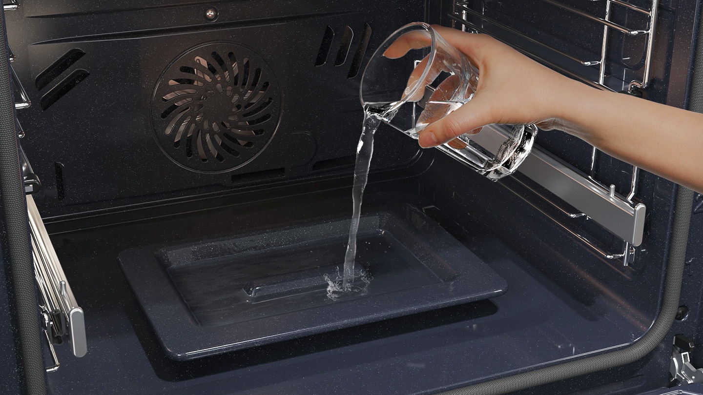 Shows a person pouring water from a glass into a dedicated tray on the bottom of the oven, which is used to create steam.