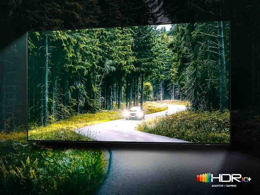 Auto běží se zapnutými světly přes les. Existuje srovnání mezi kvalitou SDR a HDR 10+ z hlediska jasu a intenzity.
