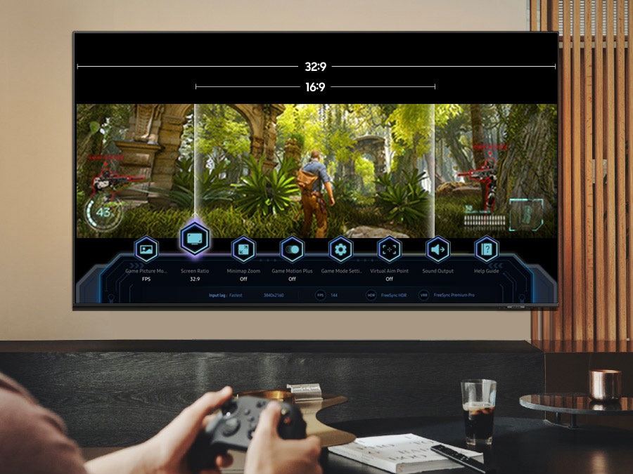 Osoba hraje hru na OLED TV, která zobrazuje herní panel a možnost přepínat mezi 32:9 a 16:9.