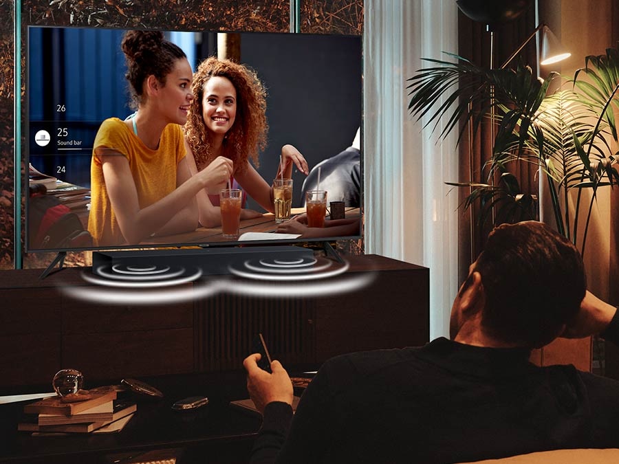 A man is watching TV at night with the Soundbar adjusted to Night Mode. The sound from the Soundbar's side speakers are emphasized during the night.