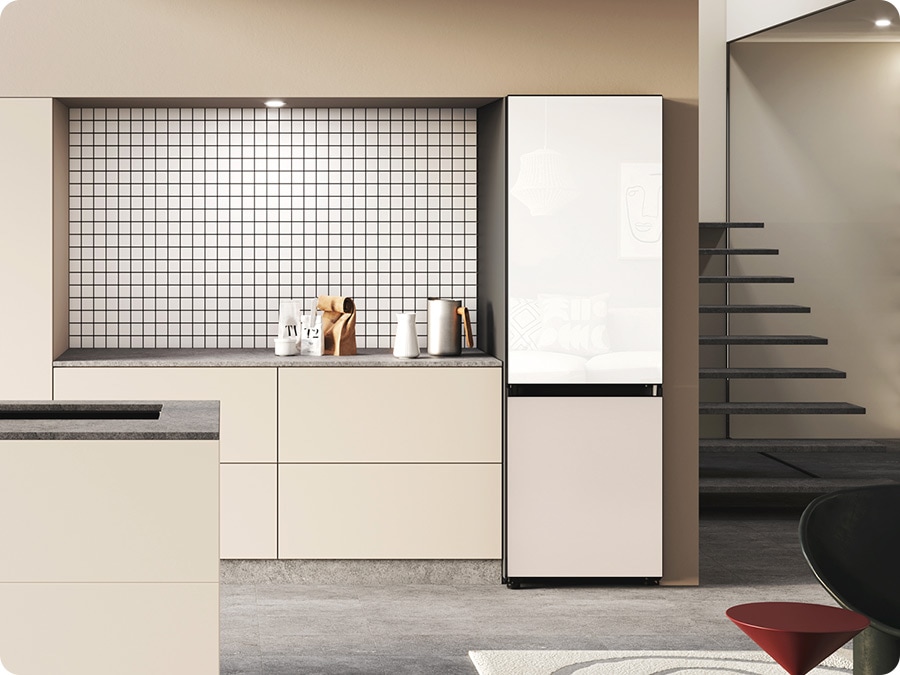 A Bespoke refrigerator with a Glam White glass top and a Satin beige glass bottom is built into a beige cabinet in a minimally decorated kitchen.