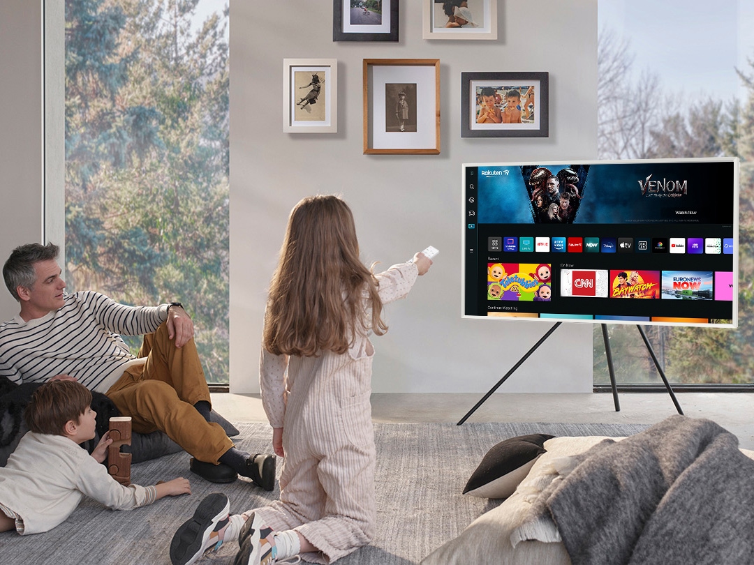 A girl is pointing the remote towards The Frame, which shows the Smart Hub home screen.