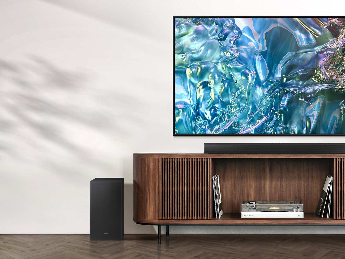 Televizor zobrazuje na obrazovce vzor modré vlny. Pod ním je TV stolek se Soundbarem nahoře a subwooferem po straně.