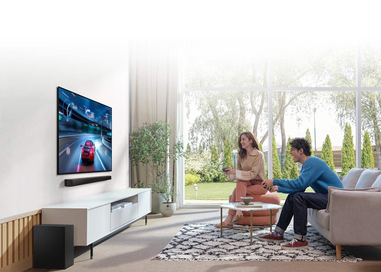 Muž a žena hrají závodní hru na svém televizoru, pod kterým je Soundbar, který poskytuje optimalizovaný zvuk s herním režimem.