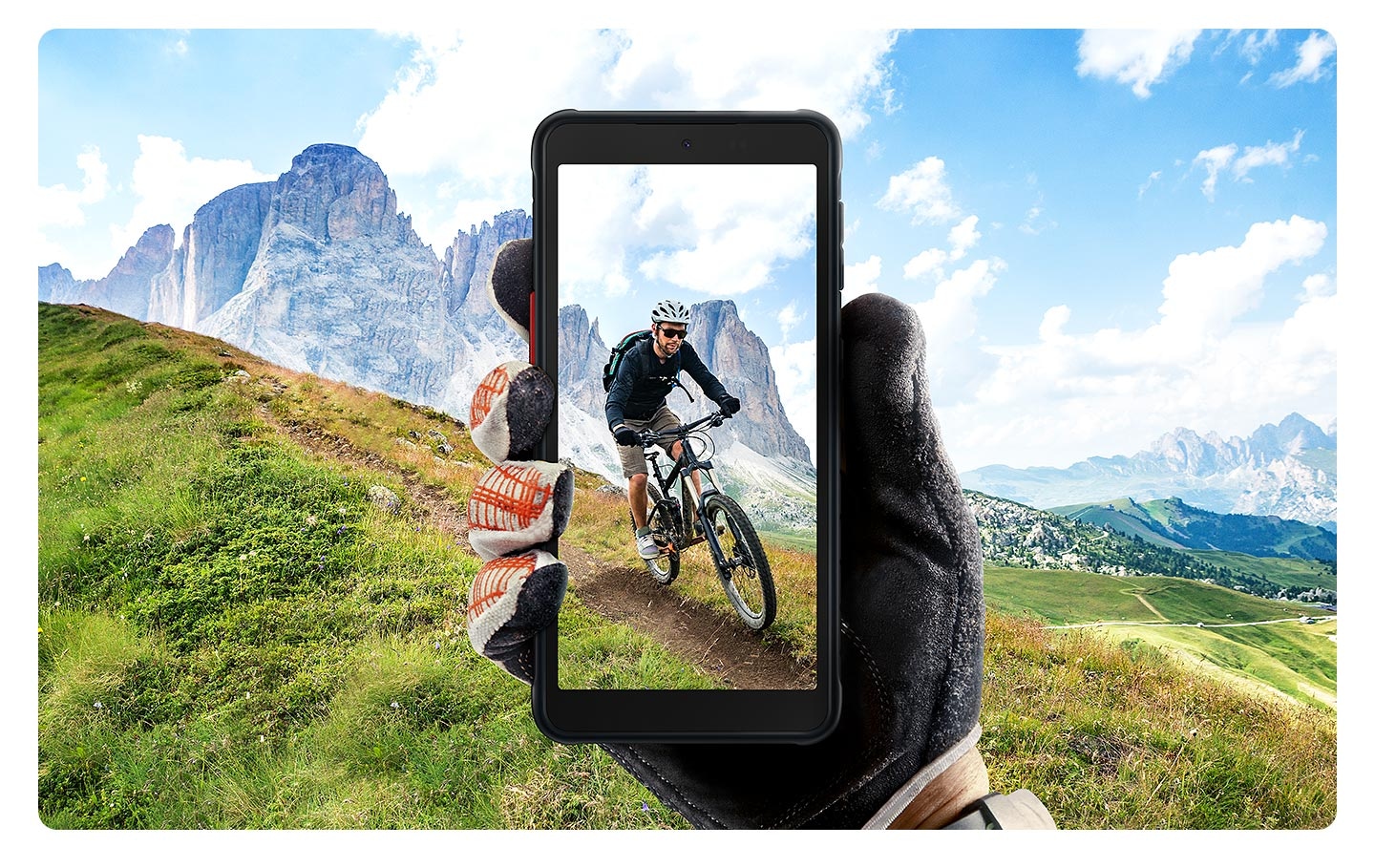 Eine Hand mit schwarzen Lederhandschuhen hält das Galaxy XCover 5, auf dessen Display eine Person beim Mountainbiken mit einem blauen Himmel im Hintergrund zu sehen ist.