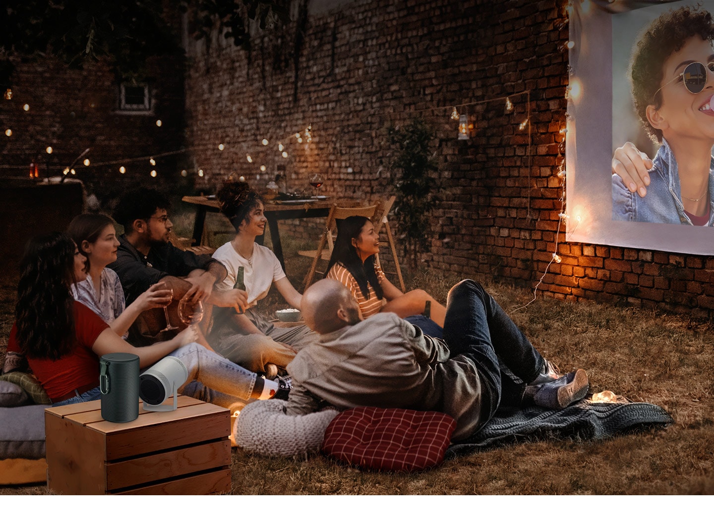 6 people on the ground are watching a projected image from the Freestyle in an outdoor setting. The case is placed next to the Freestyle.