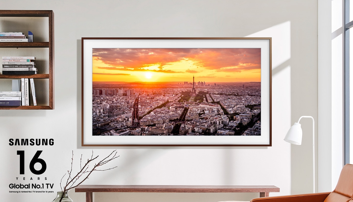 The frame is hanging on a wall in a living room displaying a sunset over a city.