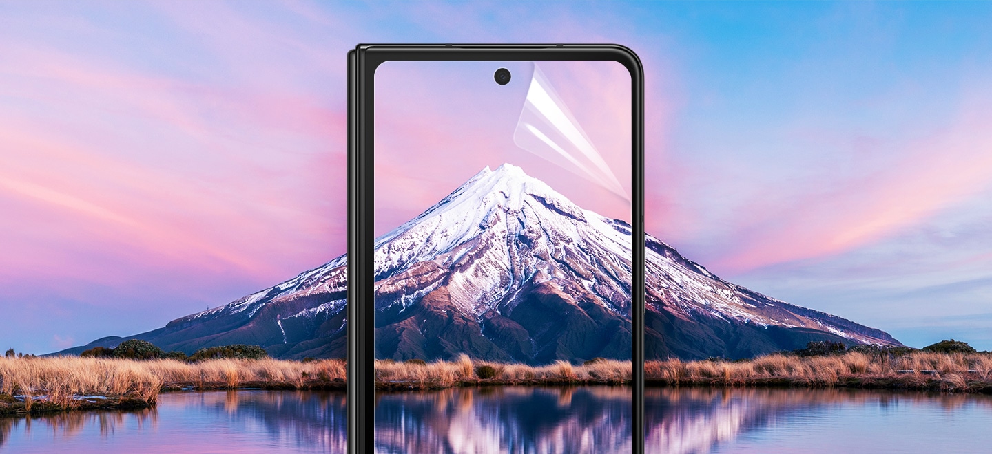 Ein Galaxy Z Fold4 Smartphone in Black zeigt auf dem Display eine schöne Berglandschaft, die sich über den Rahmen hinaus im Bildhintergrund ausbreitet. Die Displayschutzfolie auf dem Frontdisplay des Z Fold4 hat eine Ecke, die sich ablöst, um zu zeigen, dass eine Folie installiert ist.
