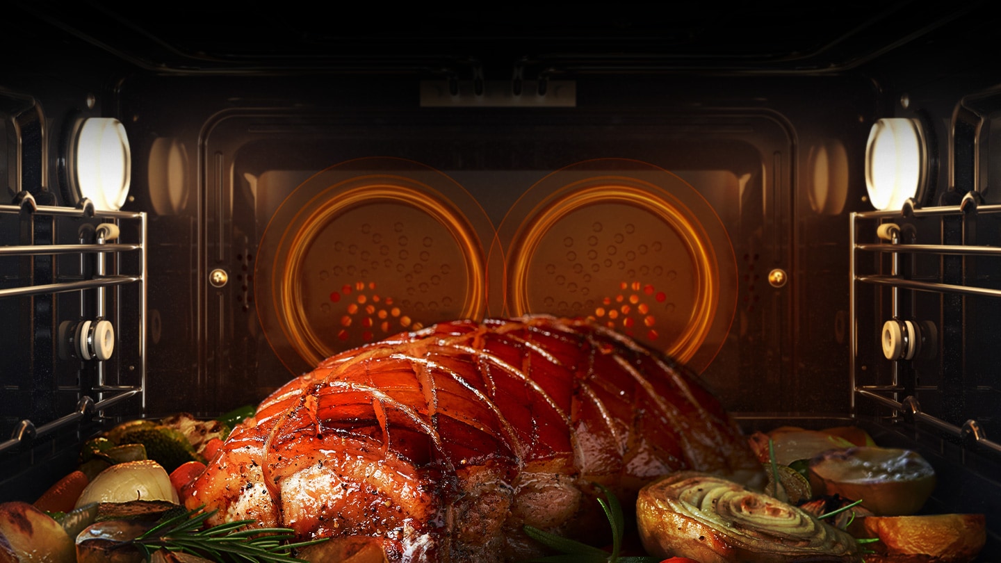Shows a joint of meat and various vegetables being roasted in the oven with dual fans at the rear circulating heat all around the oven cavity.