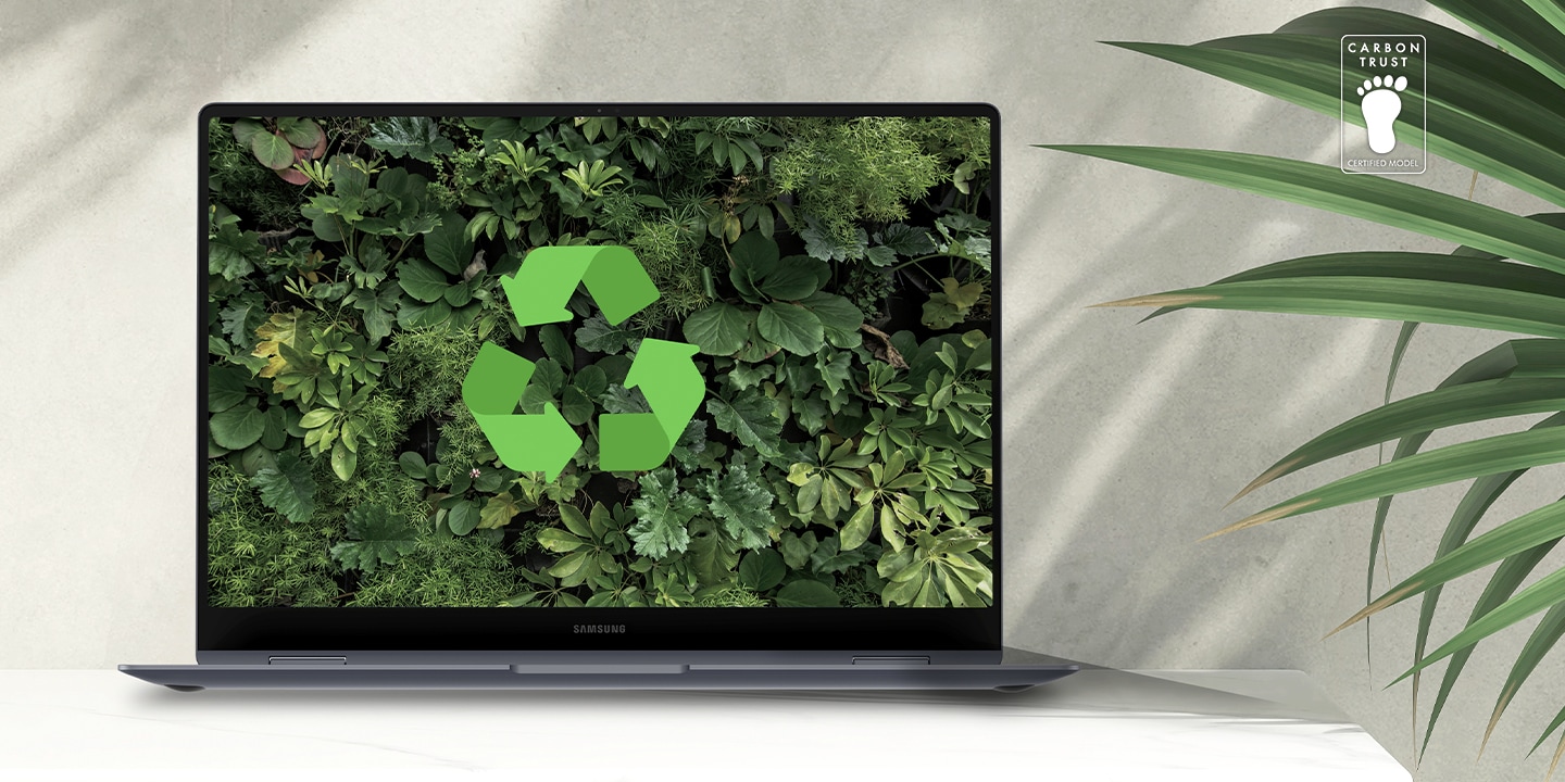 Galaxy Book4 Pro in Platinum Silver auf einem Tisch neben einer Grünpflanze, geöffnet und leicht nach rechts gerichtet, mit einer üppigen grünen Tapete und einem Recycling-Logo auf dem Bildschirm. Logo der Carbon Trust-Zertifizierung mit dem Text „CARBON TRUST. ZERTIFIZIERTES MODELL“