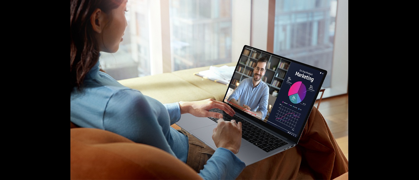 Eine Frau sitzt auf einer Couch in einem hellen Raum mit dem Galaxy Book4 Pro auf dem Schoß. Ein auf dem Bildschirm abgespieltes Video ist dank Vision Booster klar und lebendig mit verbesserter Sicht.