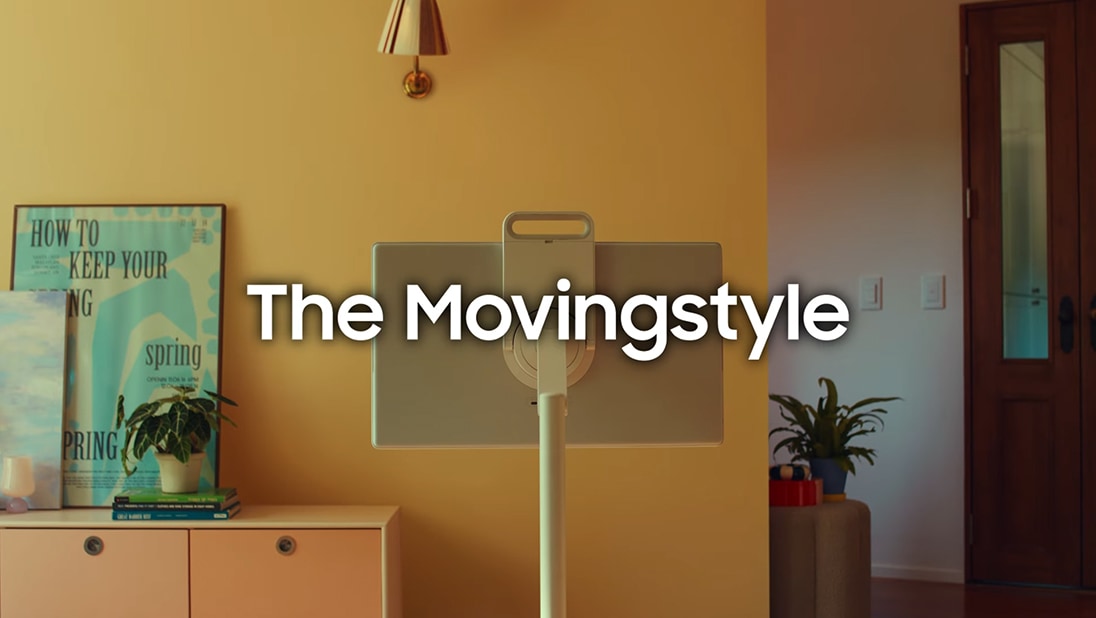 Samsung The Movingstyle steht in der Mitte eines gelben Raumes. Text „The Movingstyle“, Pflanzen und ein Poster im Hintergrund.