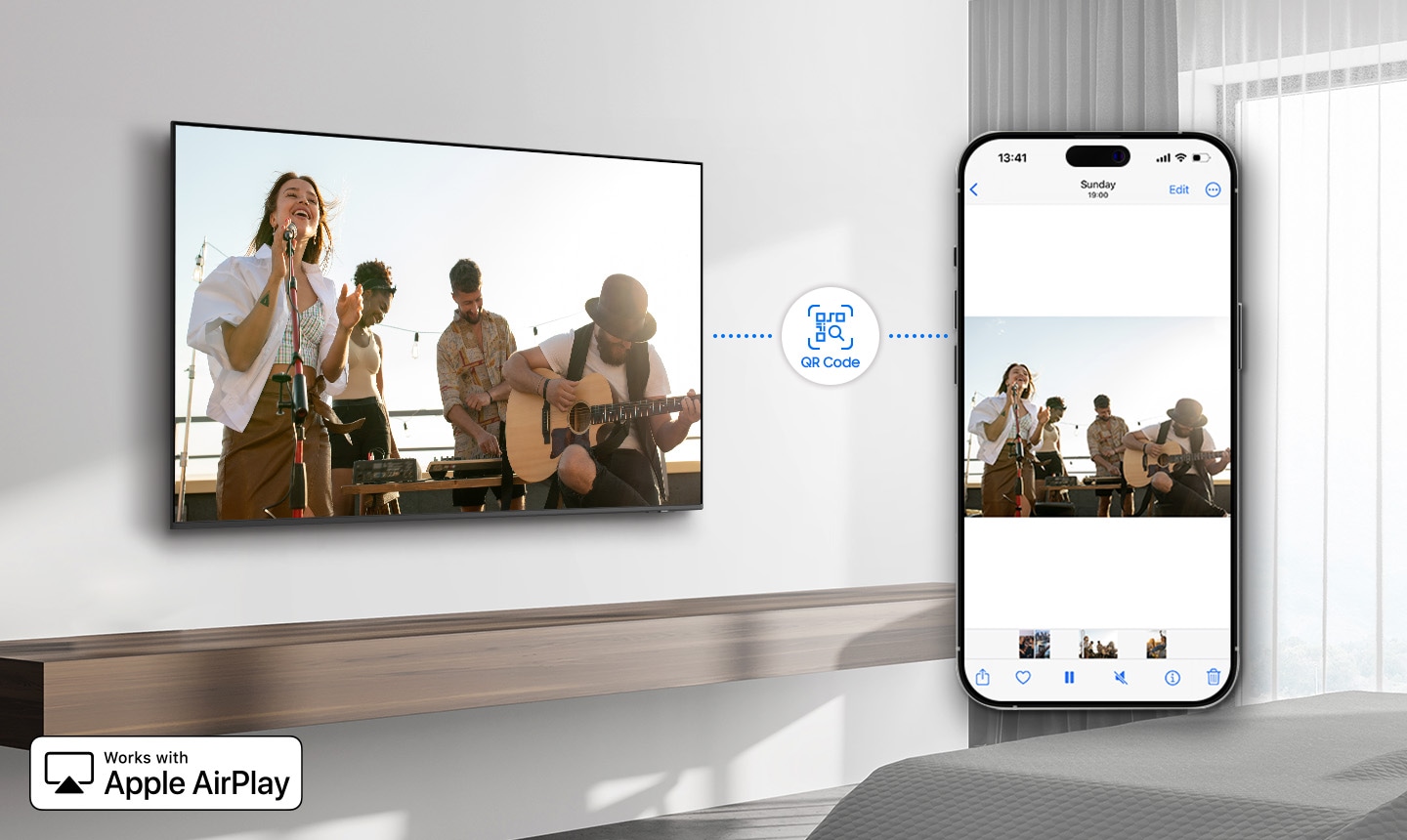 In a sunlit hotel room, the Hotel TV is mounted on the wall. This TV is connected to a smartphone via the QR Code icon and both the TV and smartphone display the same video. In the bottom left, there is a description that reads "works with Apple AirPlay".