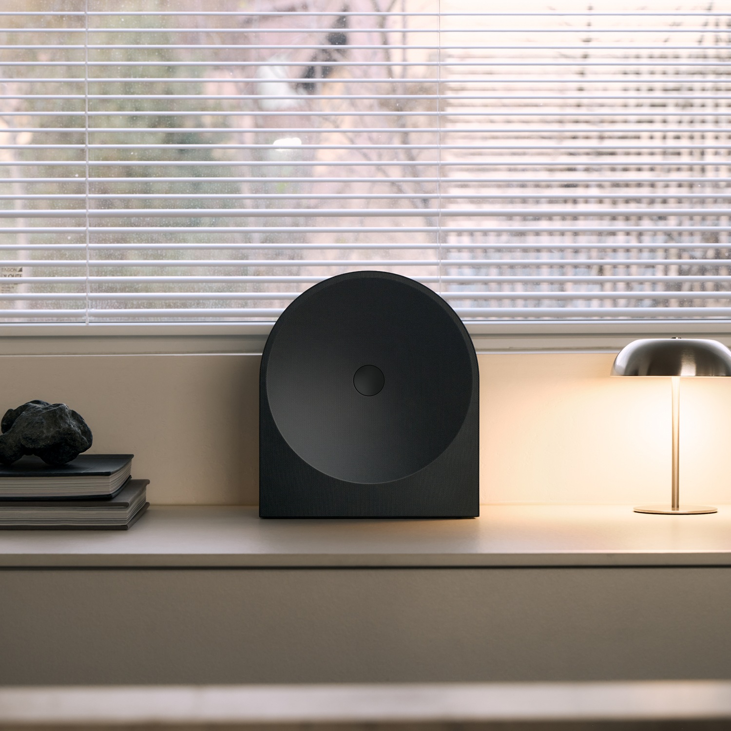 Music Studio 5‑højttaler på en træhylde i en minimalistisk stue. Den sorte, buede højttaler passer naturligt ind i indretningen ved siden af en lampe.