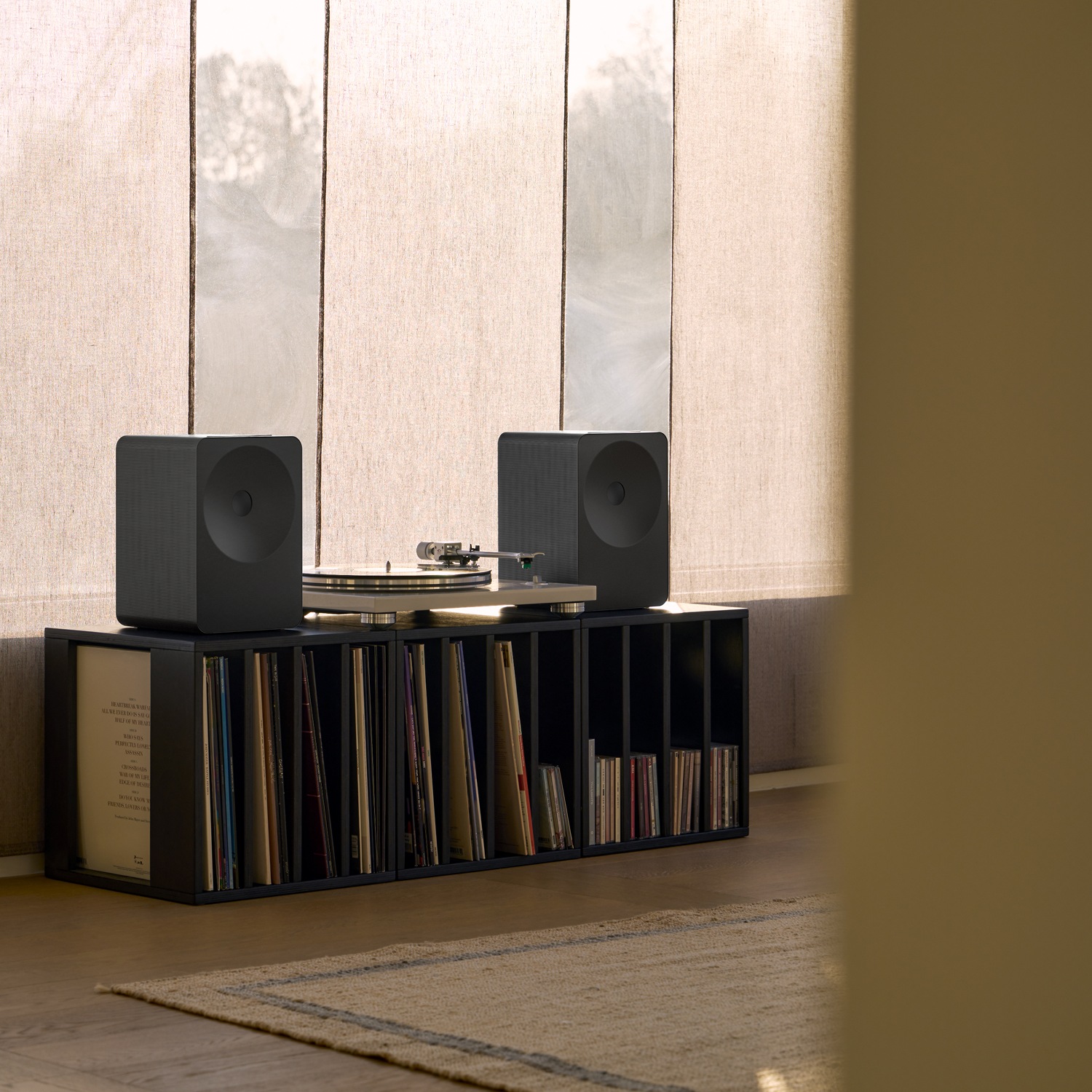 Music Studio 7‑højttaler på en træhylde ved siden af en grammofon. Højttaleren står blandt bøger og dekoration og skaber en varm, hyggelig atmosfære i en moderne bolig.