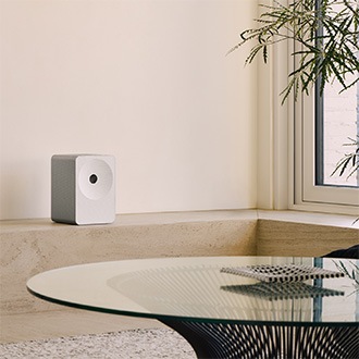 Music Studio 7-højttaler på en beige hylde. Højttaleren står blandt dekoration og en plante og skaber en varm, hyggelig atmosfære i en moderne bolig.