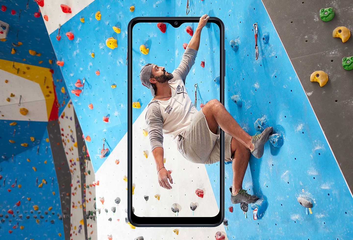 A man is doing rock climbing behind the frame of Galaxy M12.