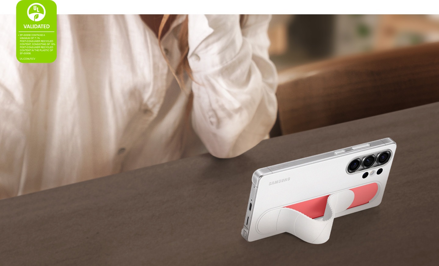 يظهر هاتف Galaxy S25 Ultra مُثبّتًا داخل غلاف Standing Grip باللون الأبيض في وضع مائل، ويُستخدم لمشاهدة الفيديوهات في الوضع الأفقي. في الزاوية اليسرى، يظهر شعار اعتماد UL Environmental Claim Validation مع نص يوضح أن الغلاف يحتوي على نسبة لا تقل عن 7.1% من المواد المعاد تدويرها بعد الاستهلاك، بما في ذلك 19% في البلاستيك المستخدم في الغلاف EF-GS938. UL.COM/ECV.