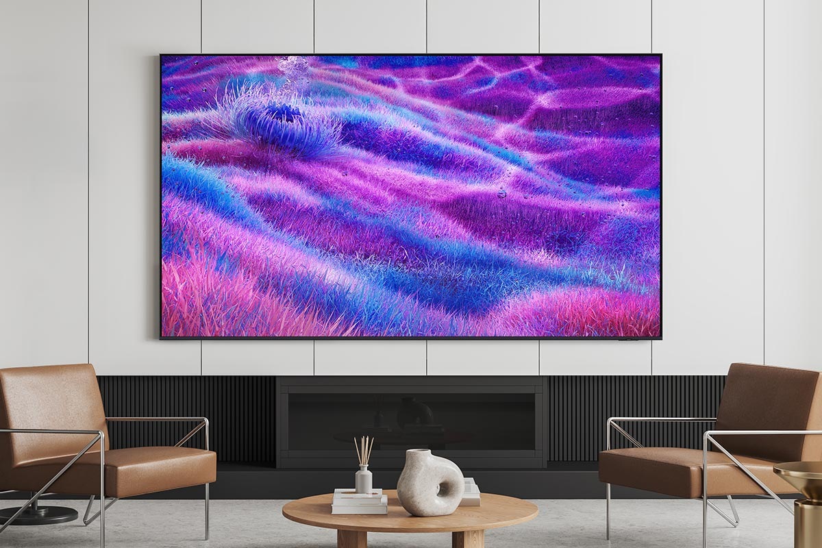 A TV is mounted on the wall in a modern living room. It displays an otherworldly grassy landscape in blue and purple colors.
