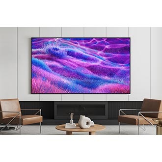 A TV is mounted on the wall in a modern living room. It displays an otherworldly grassy landscape in blue and purple colors.