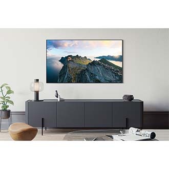 A Neo QLED TV is installed on the wall of a modern living room. The screen displays an outdoor scenes of mountains and water.