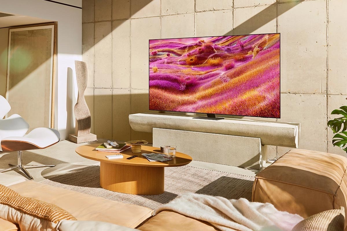 A Neo QLED TV is installed on a stand in a sunny room. The screen displays a colorful abstract landscape.