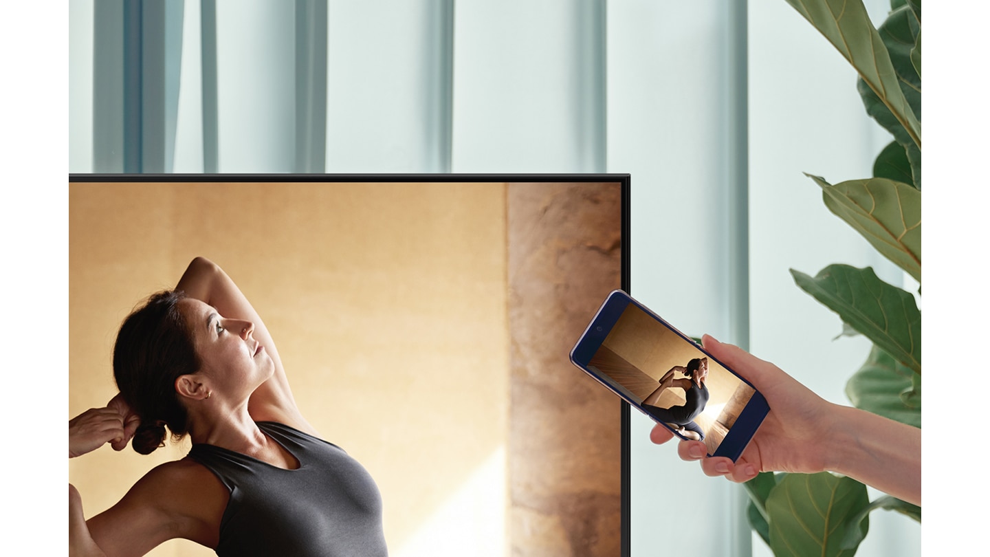 Un usuario conecta su móvil Samsung con su televisor AU7000 para reflejar el contenido de su teléfono en una pantalla más grande para mayor comodidad