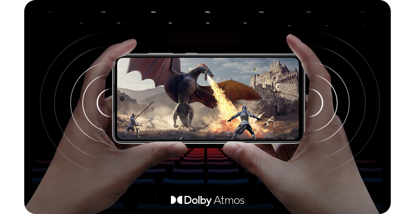 Una persona que sostiene el Galaxy A52s 5G en modo horizontal con una escena en pantalla de un caballero luchando contra un dragón que escupe fuego y ondas sonoras provenientes de ambos lados del teléfono para demostrar los parlantes estéreo. Hay un logotipo de Dolby Atmos en la parte inferior de la imagen.
