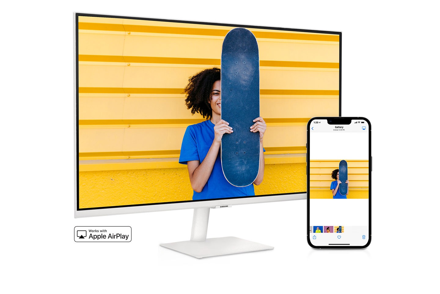 A smartphone and monitor sit side-by-side. The smartphone shows a woman posing with a skateboard. The same woman with skateboard is shown on the monitor. The smartphone's gallery app swipes through different photos which are also shown on the monitor screen.