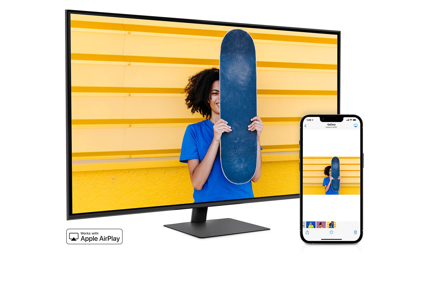 A smartphone and monitor sit side-by-side. The smartphone shows a woman posing with a skateboard. The same woman with skateboard is shown on the monitor. The smartphone's gallery app swipes through different photos which are also shown on the monitor screen.