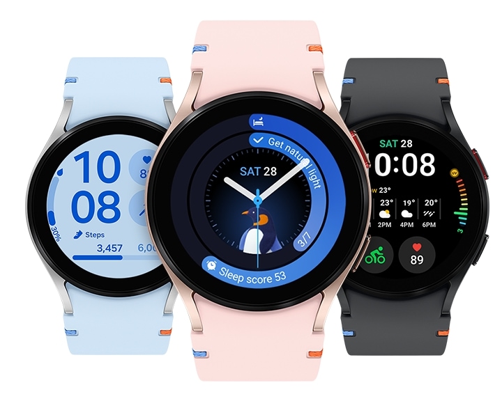 Three Galaxy Watch FEs are seen from the front. The silver watch on the left features a sky-blue stitch watch band. Its watch face displays the time, total steps, and heart rate. The pink gold watch in the middle has a pink stitch watch band. Its watch face shows the time, date, user's sleep score, and a penguin sleep animal symbol. The black watch on the right has a black stitch watch band. Its watch face shows the time, date, weather, user's heart rate, and the current exercise, which is bicycling in this case.