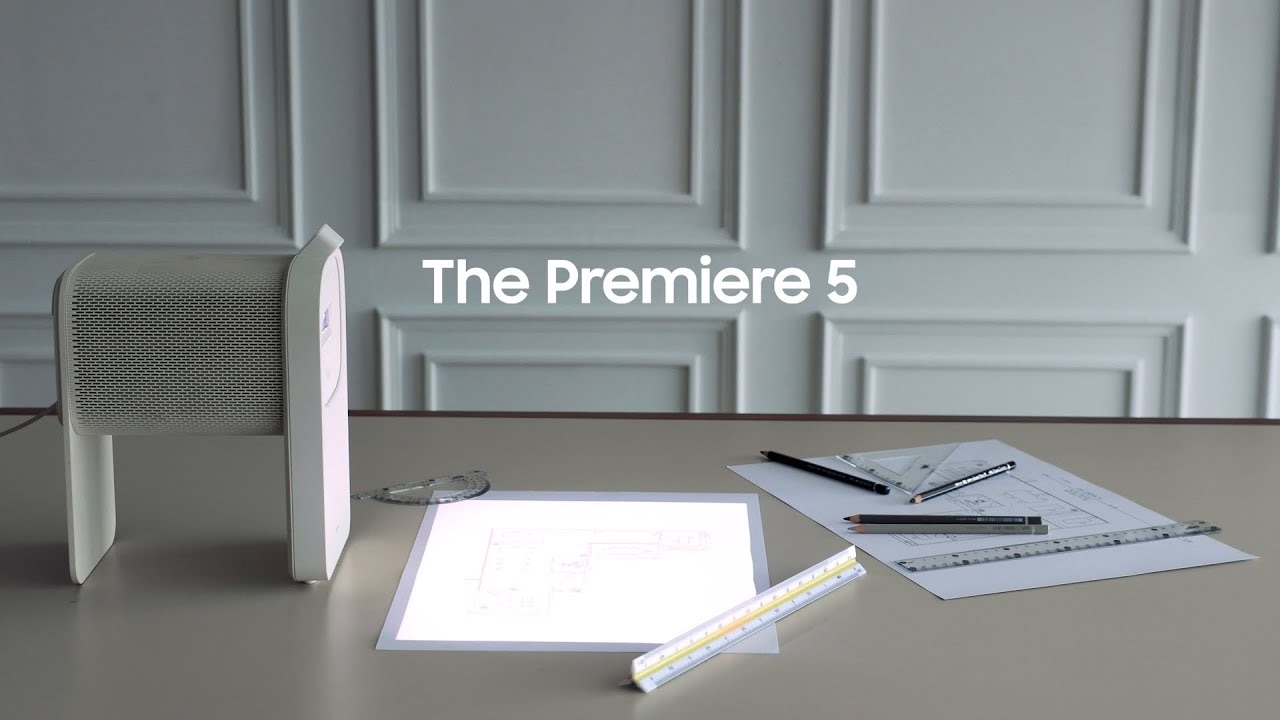 Una mujer trabaja en su escritorio con el proyector The Premiere 5 de Samsung sobre la mesa y proyecta desde su móvil algunos planos de arquitectura e interiorismo sobre ella. En otro momento, el proyector proyecta sobre la mesa el juego Candy Crush y se observan los dedos de la mujer interactuando con el juego. En la cocina, el proyector se encuentra sobre la encimera y proyecta sobre ella una videoreceta desde el móvil mientras una mujer prepara todos los alimentos.