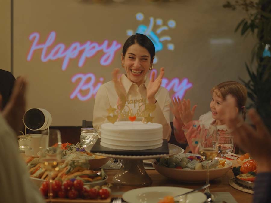 Egy boldog nő, emberek között, elfújja a tortán lévő gyertyákat. Mögötte egy születésnapi dekoráció látható a falon, amelyet a Freestyle vetített ki. A kamera kizoomol, felfedve, hogy a buli a szabadban, egy úszómedence melletti teraszon zajlik.