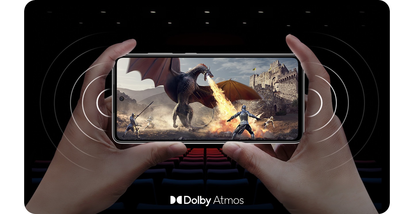 Une personne tenant le Galaxy A52s 5G en mode paysage avec une scène à l'écran d'un chevalier combattant un dragon crachant du feu, et des ondes sonores provenant de chaque côté du téléphone pour démontrer les haut-parleurs stéréo. Il y a un logo Dolby Atmos en bas de l'image.