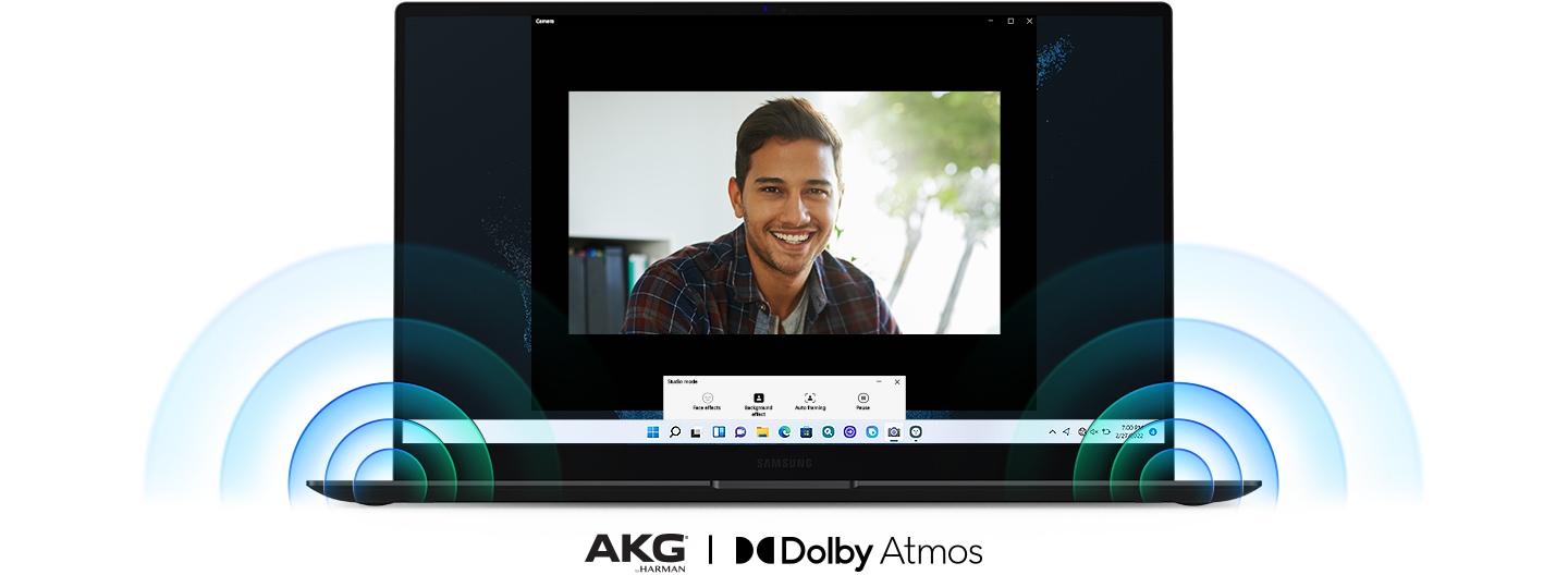 Um Galaxy Book2 Pro está aberto de frente. Na tela, um homem sorridente durante uma videochamada. Um som poderoso sai dos alto -falantes localizados nos cantos mais baixos do PC. Sob o PC, há dois logotipos para AKG® de Harman e Dolby Atmos