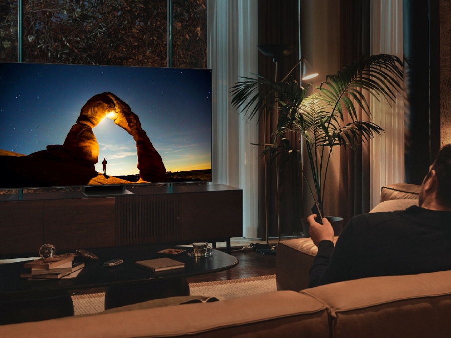 Мужчина смотрит ночью свой QLED-телевизор с экраном, оптимально настроенным на режим EyeComfort.