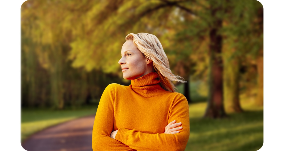 1. Une femme se tient dans un parc, les bras croisés. Elle est mise au point, et les arbres à l'arrière-plan sont légèrement flous.