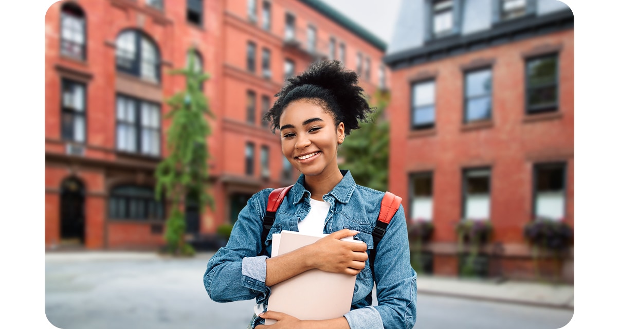 A female student, wearing a backpack and clutching onto a few books, is smiling. With the Portrait On icon above activated, she is in focus, and red brick-stoned buildings in the background are gently blurred.