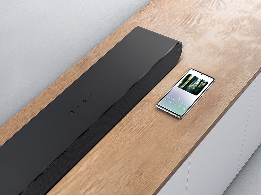 Un smartphone qui affiche un écran de musique est posé à côté d'une barre de son Samsung qui présente la connectivité Bluetooth pour la lecture de musique sur smartphone.