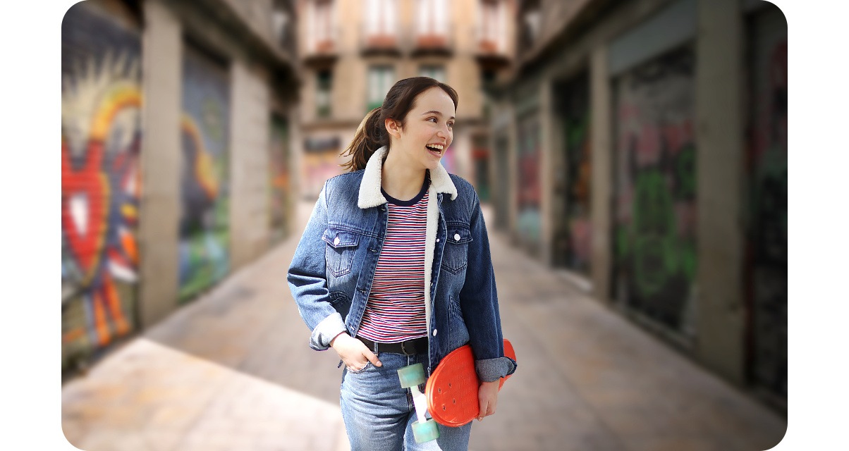 Une femme se tient devant une ruelle peinte de graffitis colorés. Lorsque le mode Portrait est activé, l'arrière-plan est flou et la photo met en valeur la femme. 