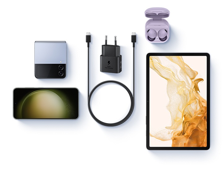 Une vue en plongée de différents appareils est présentée avec un adaptateur secteur 25W noir et un câble USB-C placés au centre. À gauche, un Galaxy Z Flip4 bleu et un Galaxy S23 sont présentés. À droite, on voit les Galaxy Buds 2 Pro en lavande et une Galaxy Tab S8.