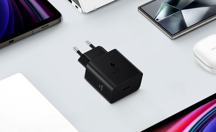 Une vue de dessus de divers appareils Samsung Galaxy est présentée avec un adaptateur d'alimentation noir placé au centre. À gauche, un Galaxy Book3, à droite un Galaxy Buds2 Pro en blanc, un Galaxy Tab S9 et un Galaxy S24 Ultra sont également montrés.