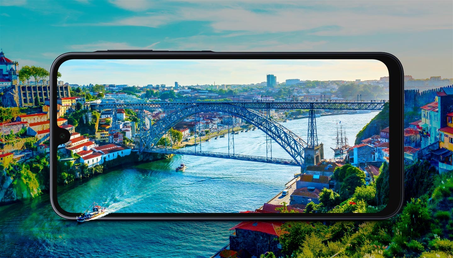 An illustration of a cityscape with a river running through and a bridge connecting two sides. A large screen of Galaxy A16 in the center displays a real photo of the scene. A boat on the river appears as if coming out of the screen, showcasing the device's immersive display quality.